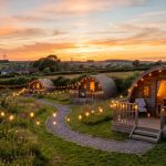 UK glamping pods in a countryside field at sunset with string lights