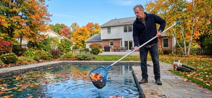 New York homeowner removing leaves from backyard swimming pool.
